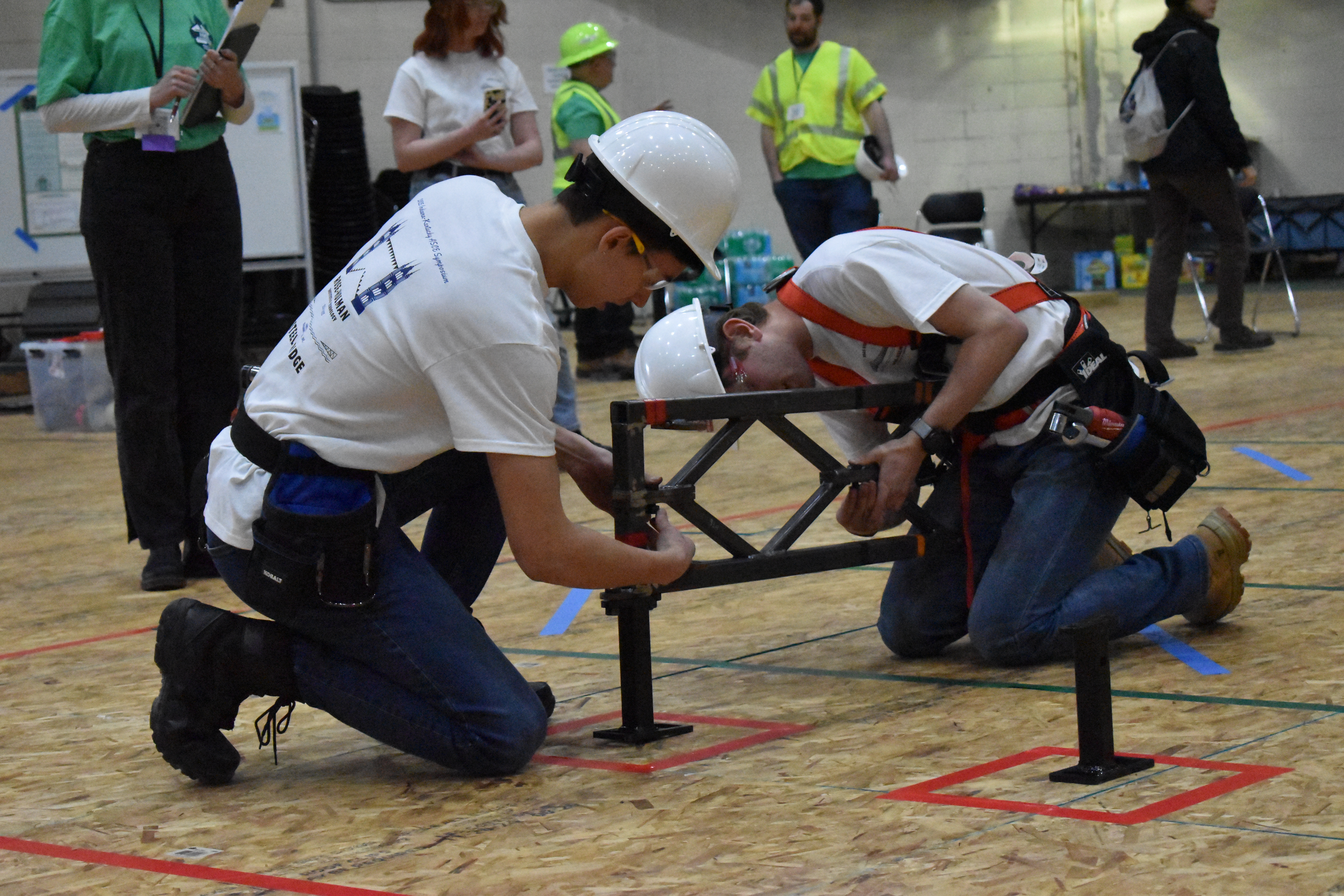 Two students kneel beside the bridge as they build.
